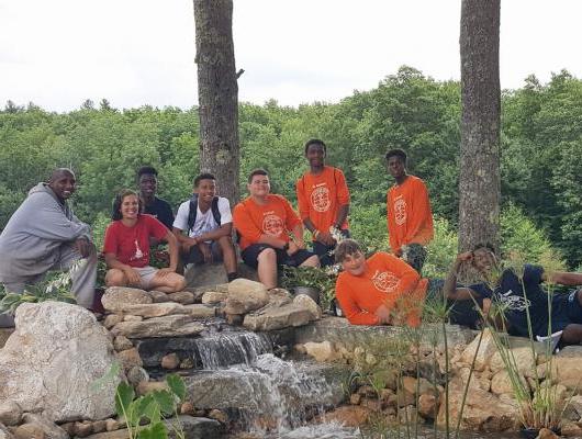 Ron Burton训练村的岩浆设计小组和一群孩子坐在瀑布旁